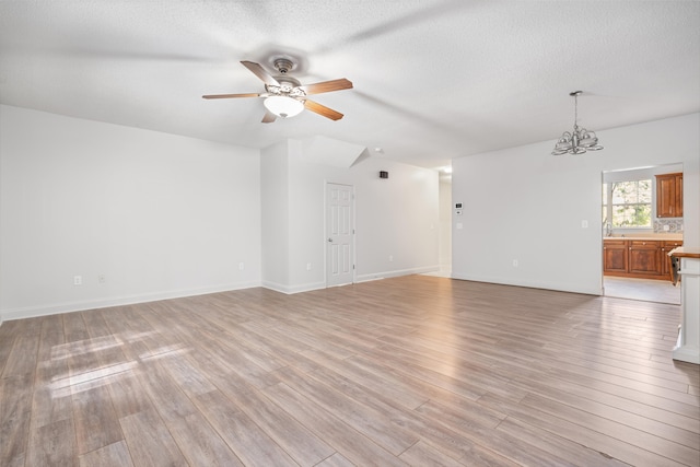 unfurnished living room with ceiling fan with notable chandelier, light hardwood / wood-style floors, and a textured ceiling