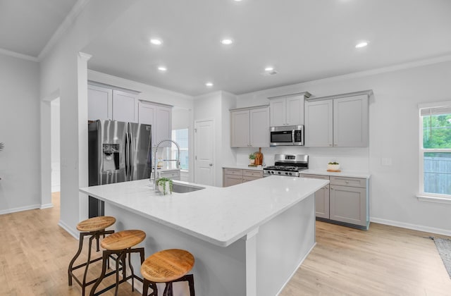 kitchen with a sink, stainless steel appliances, gray cabinets, crown molding, and a kitchen island with sink