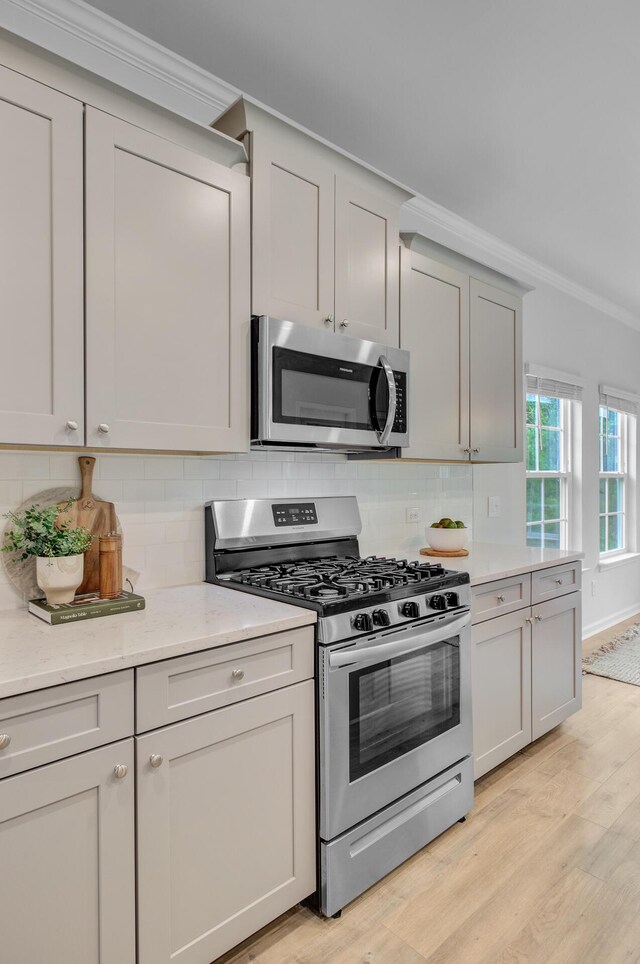 kitchen with appliances with stainless steel finishes, crown molding, light wood-style flooring, backsplash, and gray cabinetry