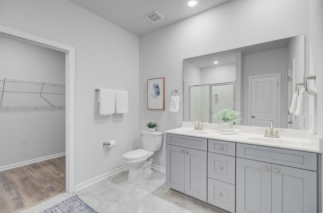 bathroom with a stall shower, toilet, double vanity, baseboards, and a walk in closet