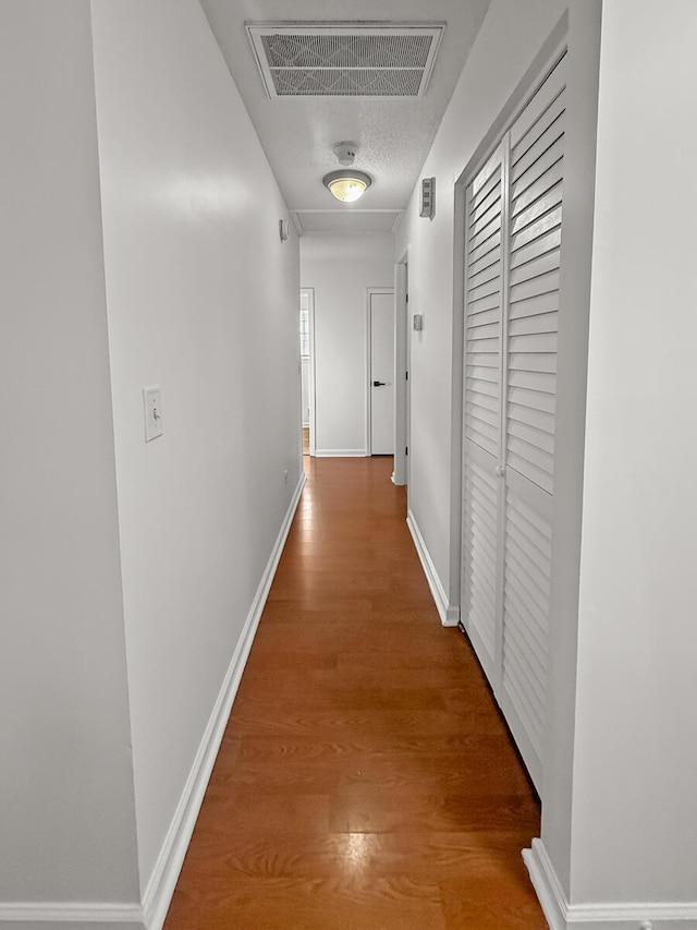 hallway with visible vents, baseboards, and wood finished floors