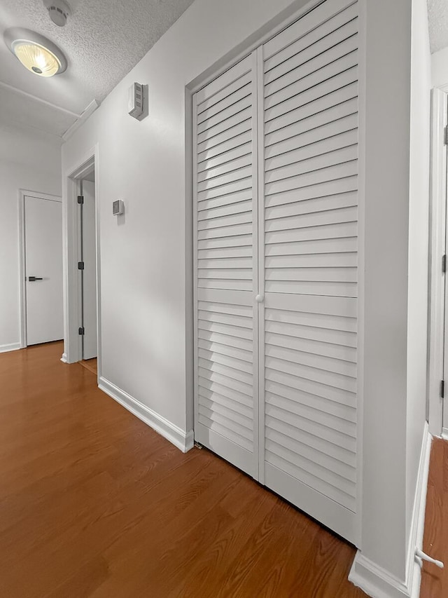 hallway with a textured ceiling, baseboards, and wood finished floors