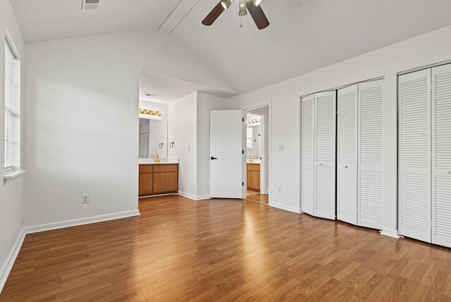 unfurnished bedroom featuring baseboards, lofted ceiling, ensuite bath, wood finished floors, and two closets