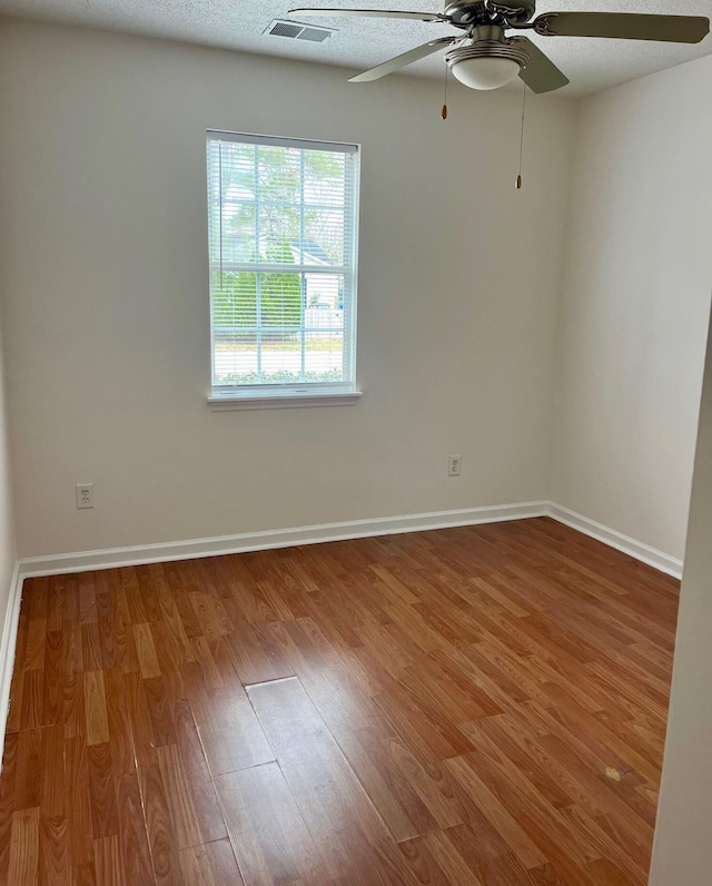 empty room with baseboards, a textured ceiling, visible vents, and wood finished floors