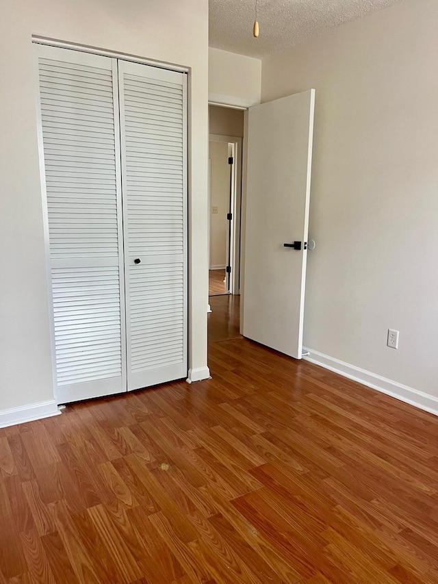 unfurnished bedroom featuring a closet, a textured ceiling, baseboards, and wood finished floors