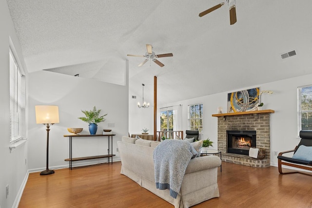 living area featuring visible vents, wood finished floors, vaulted ceiling, a fireplace, and a wealth of natural light