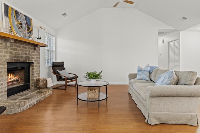 living area with lofted ceiling, a brick fireplace, wood finished floors, and visible vents