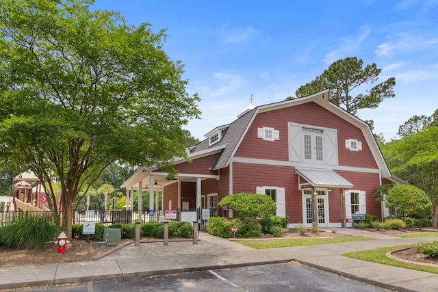 colonial inspired home with a gambrel roof, french doors, uncovered parking, a playground, and covered porch