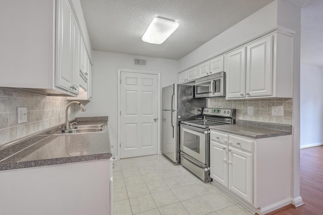 kitchen featuring sink, white cabinets, light tile patterned floors, decorative backsplash, and appliances with stainless steel finishes