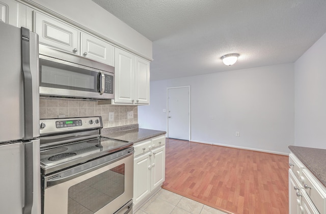 kitchen featuring a textured ceiling, light tile patterned floors, tasteful backsplash, white cabinetry, and appliances with stainless steel finishes