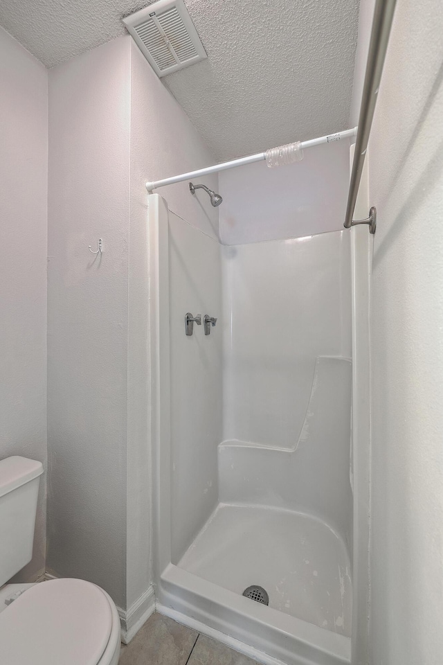 bathroom with a textured ceiling, tile patterned flooring, a shower, and toilet