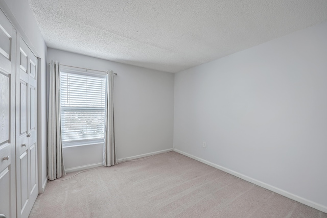 unfurnished bedroom featuring a textured ceiling, a closet, and light carpet