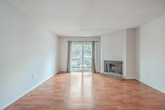 unfurnished living room with a brick fireplace, light wood-type flooring, and a textured ceiling