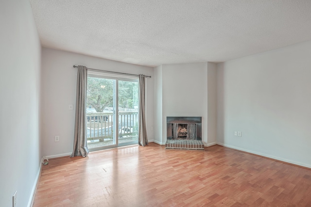 unfurnished living room featuring a fireplace, light wood-type flooring, and a textured ceiling