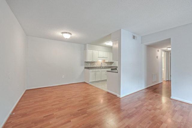 unfurnished living room featuring sink, a textured ceiling, and light hardwood / wood-style floors