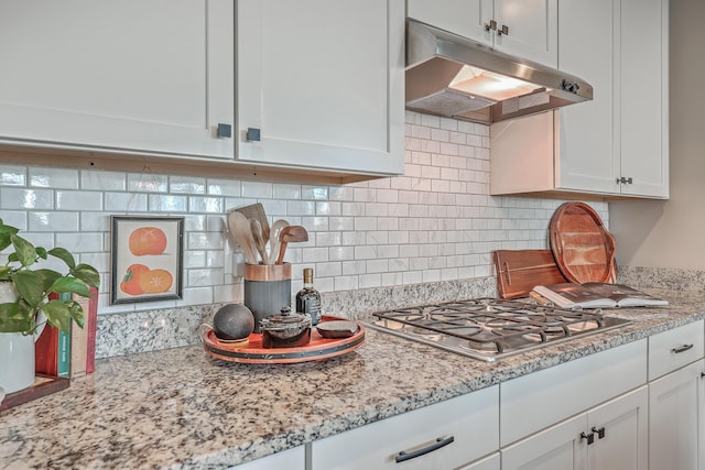 kitchen featuring light stone countertops, backsplash, white cabinetry, and stainless steel gas stovetop