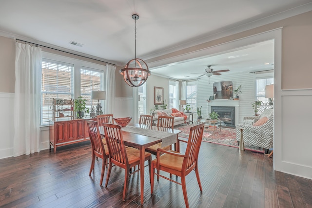 dining area with ceiling fan with notable chandelier, dark hardwood / wood-style flooring, a fireplace, and ornamental molding