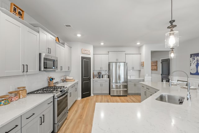 627 Macintyre Cir, Summerville, SC 29486 - kitchen featuring appliances with stainless steel finishes, a sink, decorative backsplash, decorative light fixtures, and light wood-style floors
