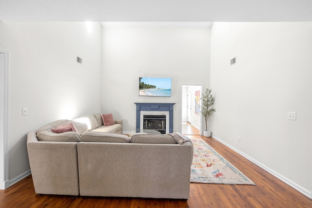 living room with a glass covered fireplace, visible vents, baseboards, and wood finished floors