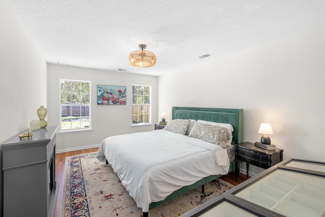 bedroom featuring baseboards, a textured ceiling, visible vents, and wood finished floors