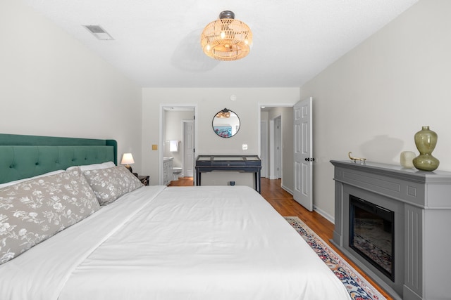 bedroom featuring ensuite bath, a fireplace, wood finished floors, and visible vents