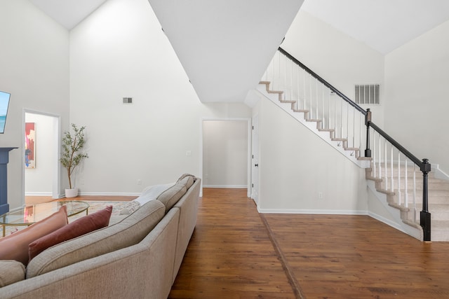 living area with stairs, visible vents, wood finished floors, and a towering ceiling