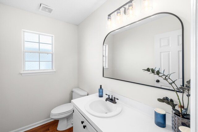 bathroom featuring baseboards, visible vents, toilet, wood finished floors, and vanity