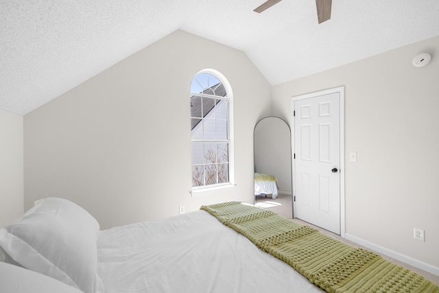 bedroom featuring a ceiling fan, vaulted ceiling, a textured ceiling, and baseboards