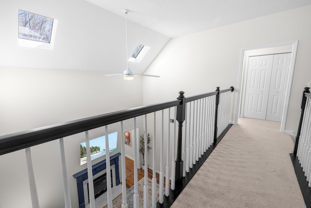 corridor with vaulted ceiling with skylight, baseboards, carpet flooring, and an upstairs landing