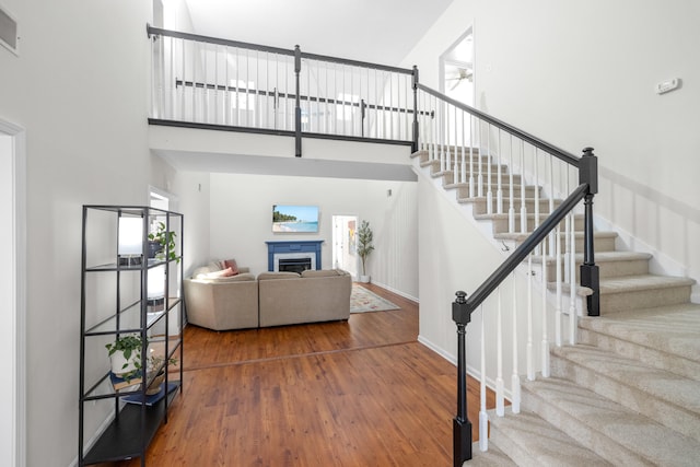 stairs featuring baseboards, visible vents, wood finished floors, a high ceiling, and a fireplace