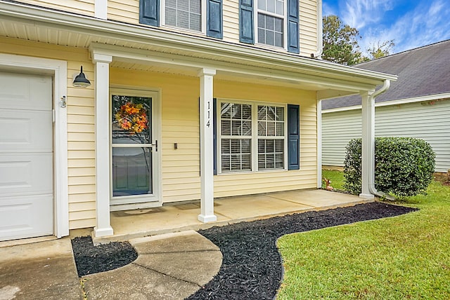 entrance to property featuring a garage, a yard, and covered porch