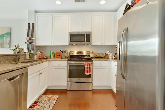 kitchen featuring white cabinetry, light stone counters, ornamental molding, appliances with stainless steel finishes, and light hardwood / wood-style floors