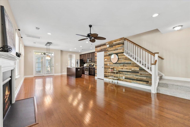 unfurnished living room with ceiling fan, wood-type flooring, sink, and wood walls