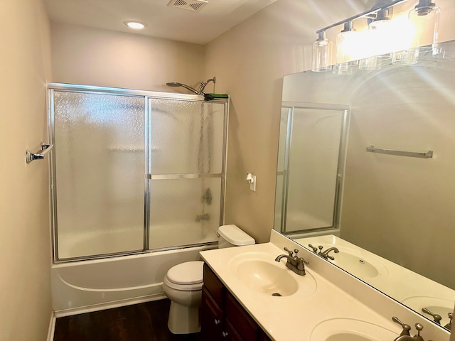 bathroom featuring toilet, double vanity, enclosed tub / shower combo, and wood finished floors
