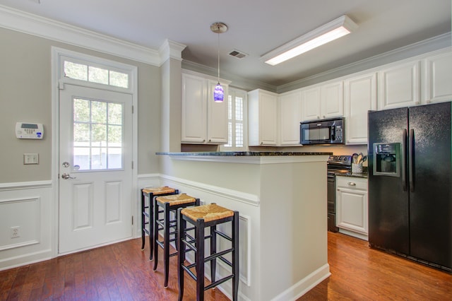 kitchen with black appliances, a kitchen bar, white cabinetry, and hardwood / wood-style flooring