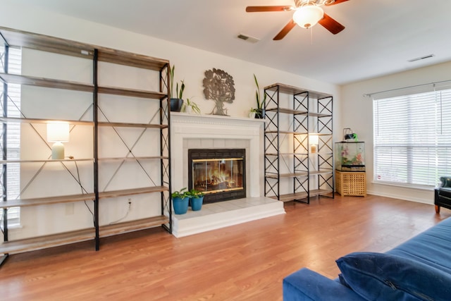 living area featuring a ceiling fan, wood finished floors, a tile fireplace, and baseboards