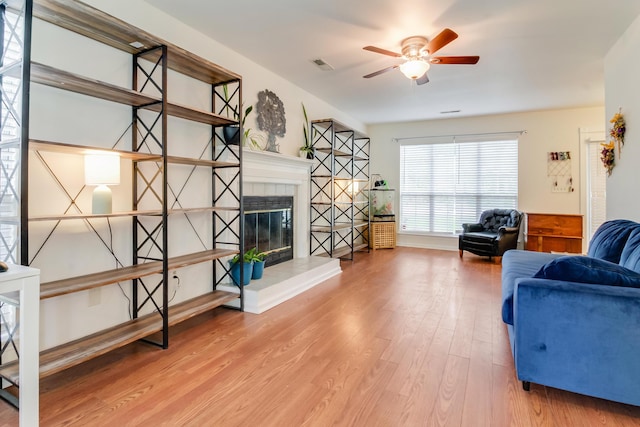 living room with wood finished floors, a ceiling fan, and a tile fireplace