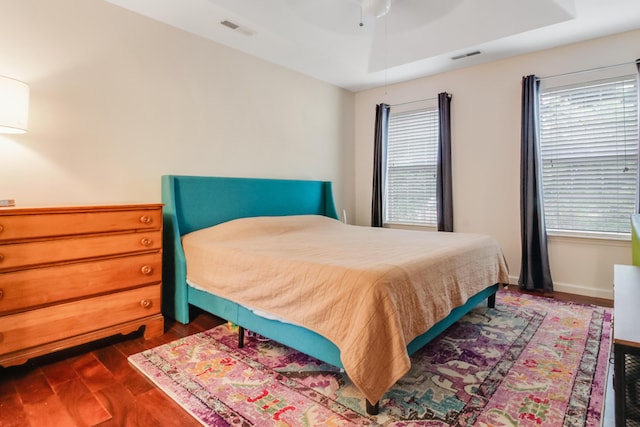 bedroom featuring dark wood-type flooring, a tray ceiling, a ceiling fan, and baseboards