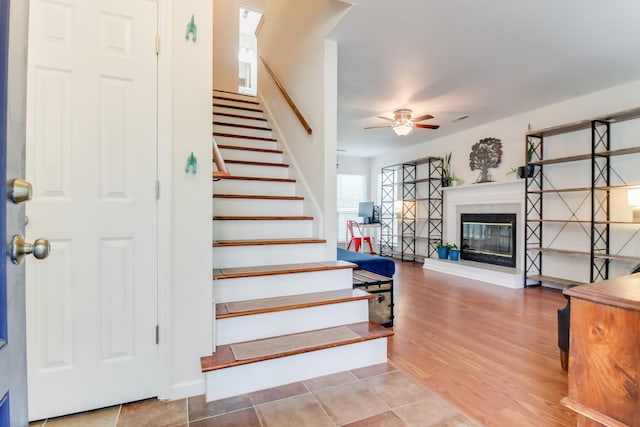 stairs featuring a ceiling fan, a tiled fireplace, wood finished floors, and baseboards