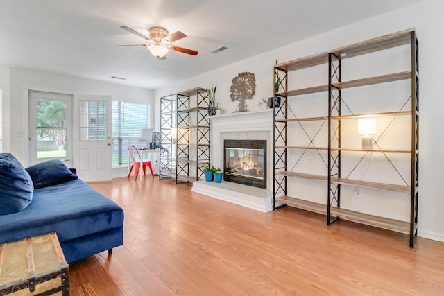 living room featuring light wood finished floors, a ceiling fan, a tiled fireplace, and baseboards
