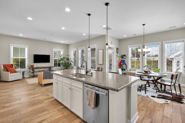 kitchen featuring stone counters, light wood-style flooring, stainless steel dishwasher, a sink, and an island with sink