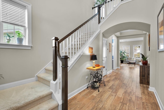 stairs with arched walkways, baseboards, a high ceiling, and hardwood / wood-style floors