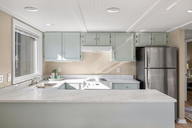 kitchen featuring stainless steel fridge, white electric range, light stone countertops, and sink