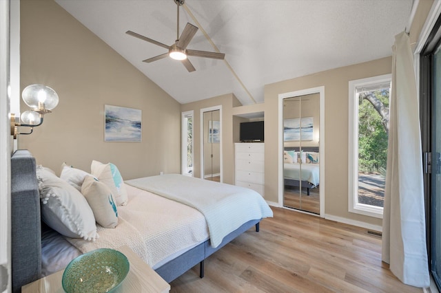 bedroom featuring multiple closets, ceiling fan, vaulted ceiling, and light wood-type flooring