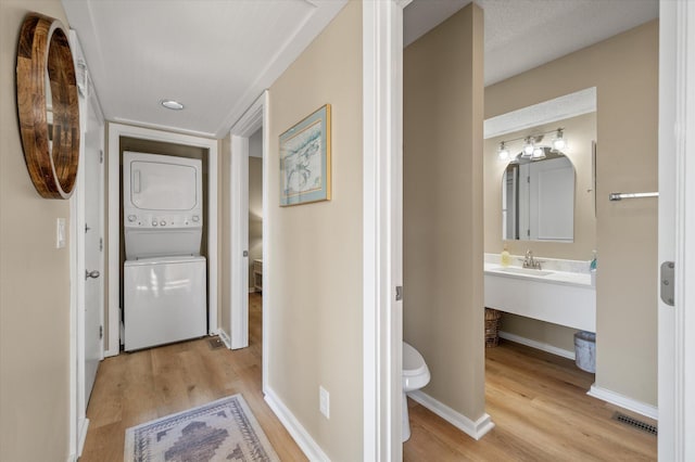 hall with sink, stacked washer / dryer, and light hardwood / wood-style flooring