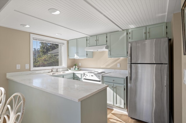 kitchen with white range with electric stovetop, stainless steel refrigerator, light stone counters, and kitchen peninsula