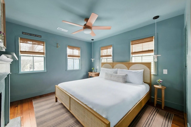 bedroom with baseboards, multiple windows, visible vents, and wood finished floors