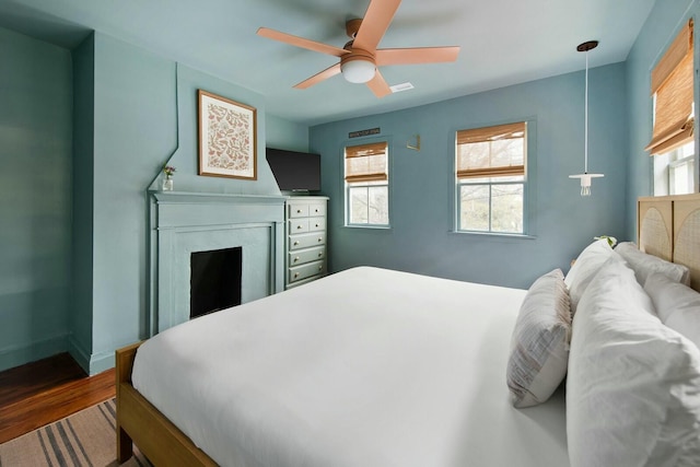 bedroom with a ceiling fan, a fireplace, baseboards, and wood finished floors