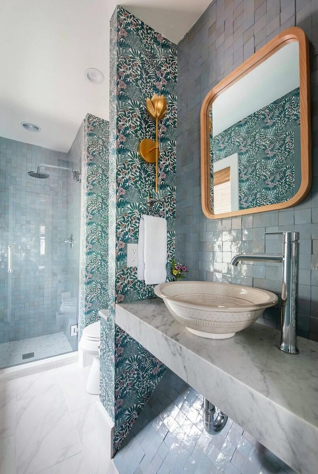 bathroom featuring toilet, a stall shower, tile walls, and a sink