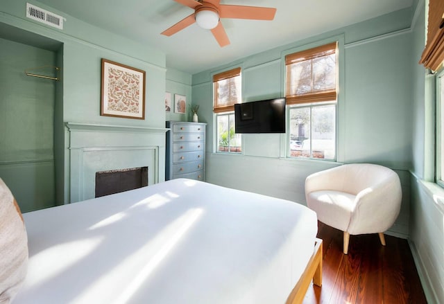 bedroom featuring ceiling fan, a fireplace, visible vents, and dark wood finished floors